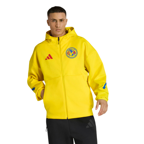 A man models a bright yellow Club América Adidas zip-up hoodie with the team crest and black pants against a solid black background.