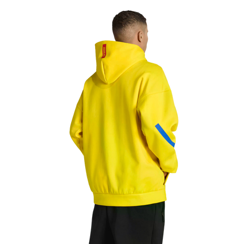 Rear view of a man in a bright yellow hoodie with a red tag and blue sleeve stripe, wearing black pants against a solid black background.