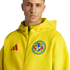 A man wears a yellow Adidas hoodie with the Club América crest against a black background.