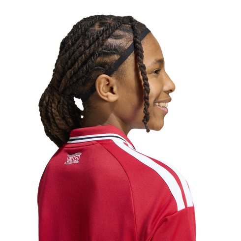 Profile of a smiling child with dark hair in twists, wearing a red and white "UNITED" athletic jacket against a white background.
