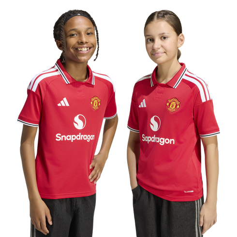 Two children smile in matching red Manchester United football jerseys with the Snapdragon logo against a white background.