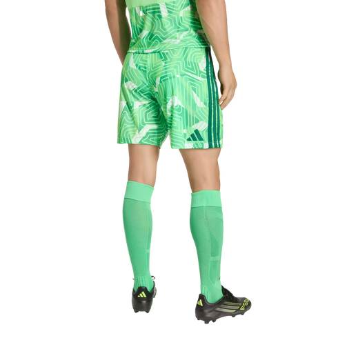 Rear view of a person wearing a green geometric-patterned Adidas soccer uniform, bright green calf-high socks, and black Adidas soccer cleats against a black background.