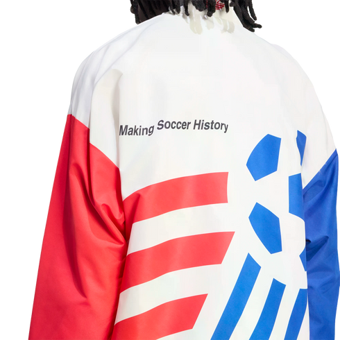 A close-up view from behind of a person wearing a white, red, and blue athletic jacket against a black background. The text "Making Soccer History" is printed in black on the white upper back. The lower back features red horizontal stripes on the left and