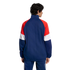 Back view of a man with curly hair wearing a navy, red, and white color-blocked track jacket and matching pants against a black background.