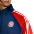 A person wears a navy blue and red FC Bayern München track jacket with the club's crest on the chest and white stripes on the sleeves.