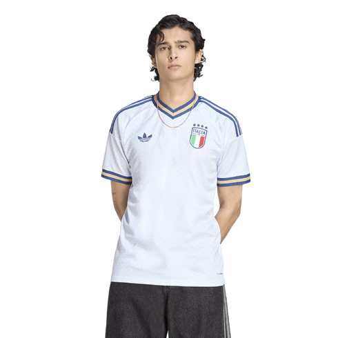 A man in a white Adidas Italy jersey with blue and gold trim, standing against a black background.