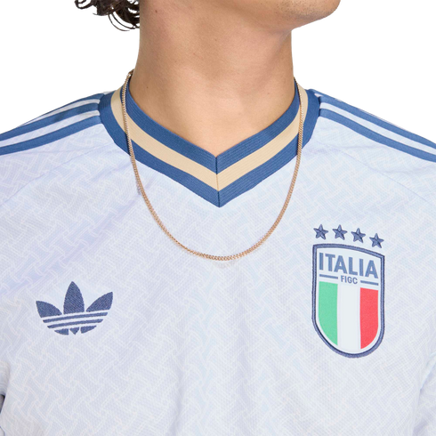 Close-up of a white Adidas Italy national team jersey featuring the FIGC crest, blue trefoil logo, and a blue and tan striped V-neck collar.