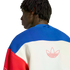 A back view of a person with dreadlocks wearing a blue, white, and red color-blocked Adidas sweatshirt with a large red Trefoil logo outline on the back.
