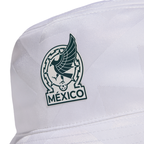 A close-up of a white bucket hat featuring a dark green and white patch. The patch depicts a stylized Aztec eagle, a soccer ball, and the word "MÉXICO" at the bottom.