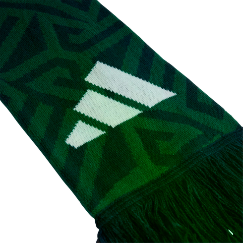 Close-up of a green knitted scarf with a white three-stripe logo, dark geometric patterns, and a fringed edge against a black background.
