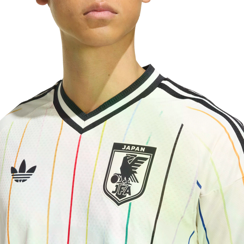 Close-up of a white Adidas Japan jersey with thin vertical rainbow stripes, featuring the Trefoil logo and JFA crest.