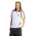A woman in a white Germany national team soccer jersey and dark pants poses against a white background. Her hair is long and braided. Her hands are in her pockets as she looks at the camera.