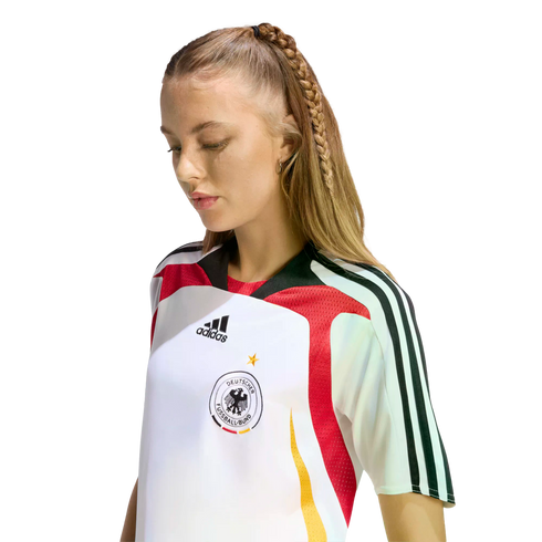 A woman with a long blonde braid looking down while wearing a white Adidas Germany national team soccer jersey.