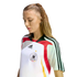 A woman with a long blonde braid looking down while wearing a white Adidas Germany national team soccer jersey.