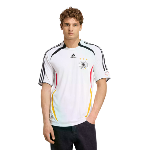 A man models a white Adidas Germany national soccer team jersey and dark jeans against a plain white background.