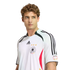 A man with curly hair wearing a white Adidas Germany national football team jersey, looking off to the side against a white background.