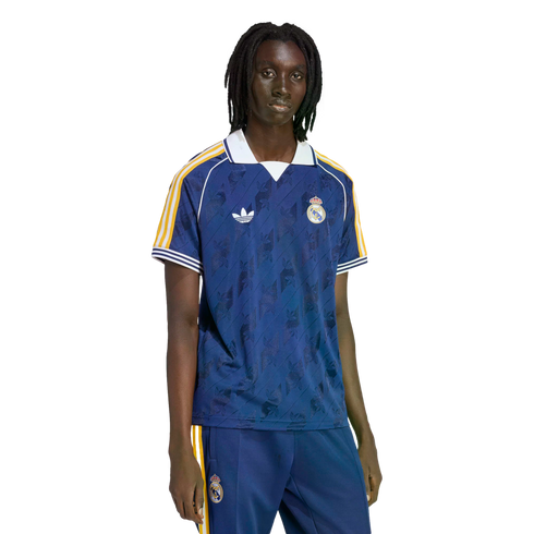 A person with dreadlocks wearing a navy blue Real Madrid soccer jersey and matching track pants against a black background.