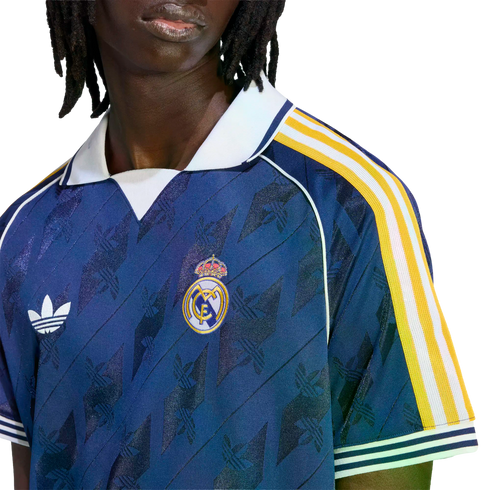 Close-up of a person wearing a navy blue Adidas Real Madrid soccer jersey with white and yellow sleeve stripes and a white polo collar.