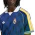 Close-up of a person wearing a navy blue Adidas Real Madrid soccer jersey with white and yellow sleeve stripes and a white polo collar.
