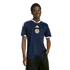 A young Black man models a navy blue Adidas Scotland soccer jersey against a solid black background.