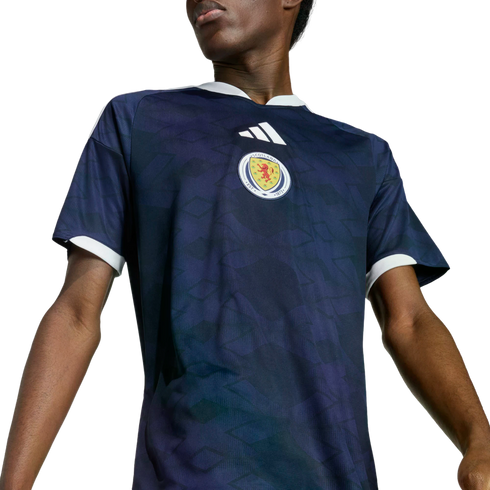 Person wearing a dark blue Adidas Scotland national football team jersey with white trim and a faint diamond pattern, set against a black background.
