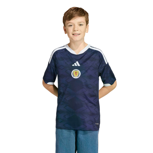 A young boy smiles while wearing a navy blue Scotland national football team jersey against a black background.