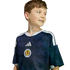A smiling young boy wearing a navy blue Scotland soccer jersey with white stripes, looking to the side against a black background.