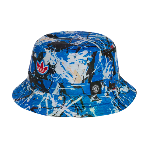 Adidas bucket hat featuring a blue and white paint-splatter design, a red trefoil logo, and a small Manchester United crest tag on a black background.