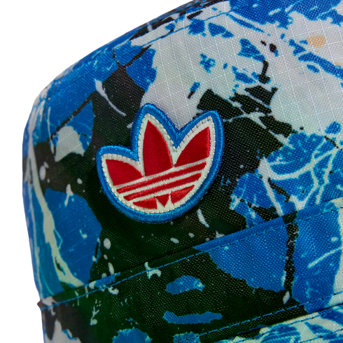 Close-up of an Adidas cap featuring an abstract blue and white splatter pattern and an embroidered red and white Trefoil logo.