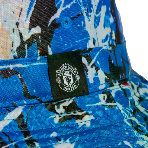 Close-up of a blue and white splash-patterned bucket hat featuring a black label with the white Manchester United crest.