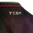Close-up of a black jersey's back neck, showing white blocky "FCBM" text below a collar with green, navy, and red checkered patterns.
