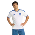A man in a white Greece national team soccer jersey with blue trim stands with hands on his hips against a black background.