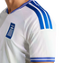 Close-up of a white athletic jersey with blue stripes on the shoulder and sleeve. A blue chest patch displays the Greek flag and the word "ΕΛΛΑΣ".