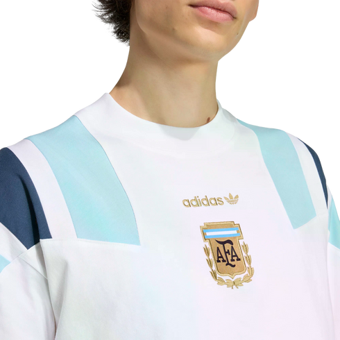 Close-up of a white Adidas sweatshirt featuring light blue shoulder panels and a gold embroidered Argentina Football Association (AFA) crest on the chest.