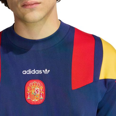 Close-up of a navy blue Adidas sweatshirt with red and yellow shoulder panels and the Spanish national football team crest on the chest.