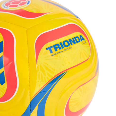 A close-up of a yellow Trionda Club replica soccer ball featuring red and blue patterns and a Colombian Football Federation logo.