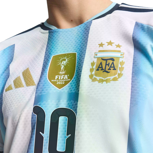 Close-up of an Argentina football jersey with blue and white stripes, featuring the FIFA World Champions 2022 patch, three-star AFA crest, and part of the number 10.