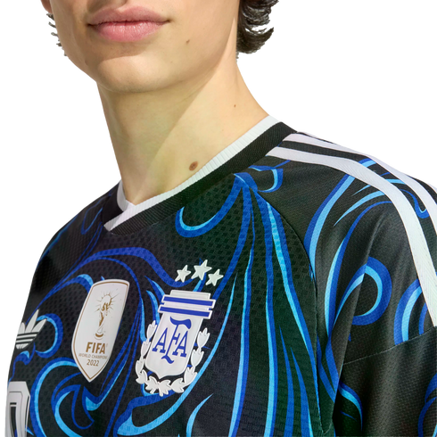 Close-up of a person wearing a black and blue patterned Argentina football jersey, featuring the AFA crest with three stars and the FIFA World Champions 2022 gold patch.