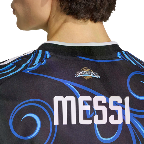 Back view of a dark soccer jersey with blue swirls, featuring the name "MESSI" in large white letters below an Argentina logo with a gold sun.