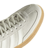 Close-up of a light grey suede sneaker with white laces, side stripes, and a textured gum rubber outsole.