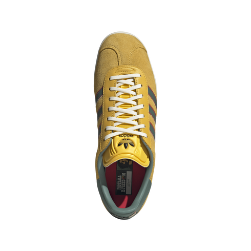 Top-down view of a yellow Adidas sneaker with white laces, green and red stripes, and a red insole reading "FOOTBALL IS FREEDOM" against a black background.