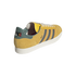 A mustard yellow suede sneaker with teal and red accents, featuring "Bob" script and a portrait on the heel tab, presented against a black background.