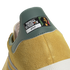 Close-up of a yellow suede shoe's green heel tab with a graphic patch reading "FOOTBALL IS FREEDOM," featuring Bob Marley’s portrait and signature.