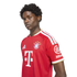 A young man posing in a red FC Bayern Munich soccer jersey with white and gold accents against a plain white background.