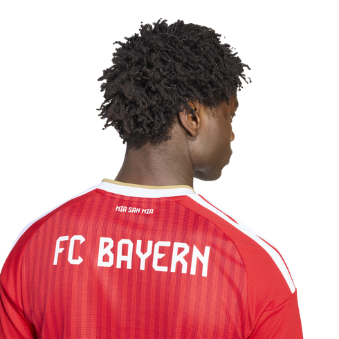 Back view of a person with dark curly hair wearing a red striped FC Bayern soccer jersey with white "FC BAYERN" and "MIA SAN MIA" lettering.