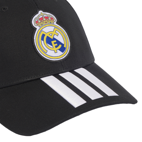 A black baseball cap featuring the Real Madrid club crest on the crown and three white Adidas stripes on the visor.