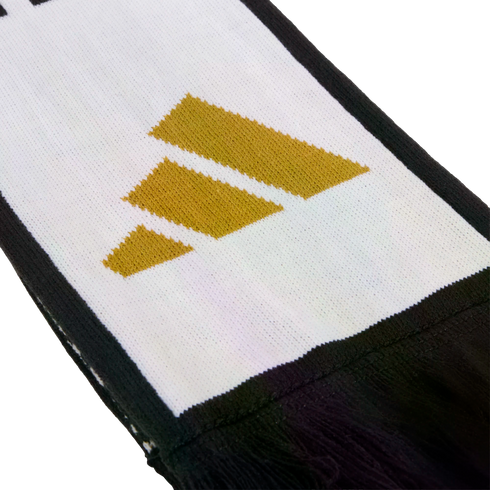 Close-up of a white knitted scarf with a black border, featuring a gold three-stripe logo and black fringes at the end.