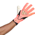 A dark-skinned arm wearing a pink, black, and white goalkeeper glove with gold accents, set against a plain white background.