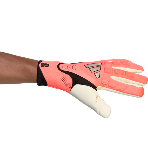A pink and black Adidas goalkeeper glove with "URG 2.0+" branding, worn on a left arm and shown horizontally against a white background.