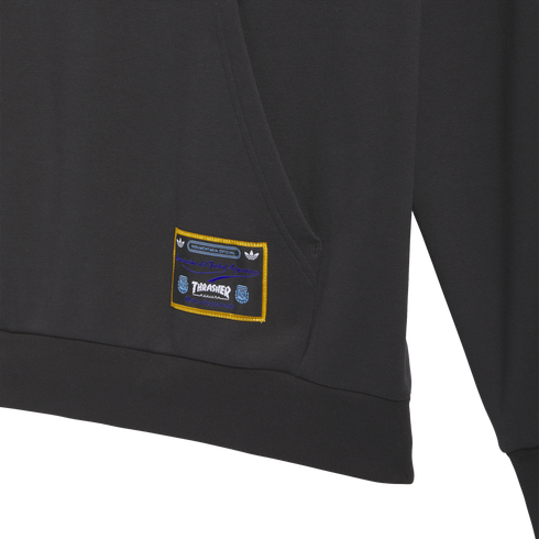 Close-up of a dark gray hoodie with a woven rectangular patch. The patch has a gold border and includes the Thrasher logo and Argentine Football Association text.